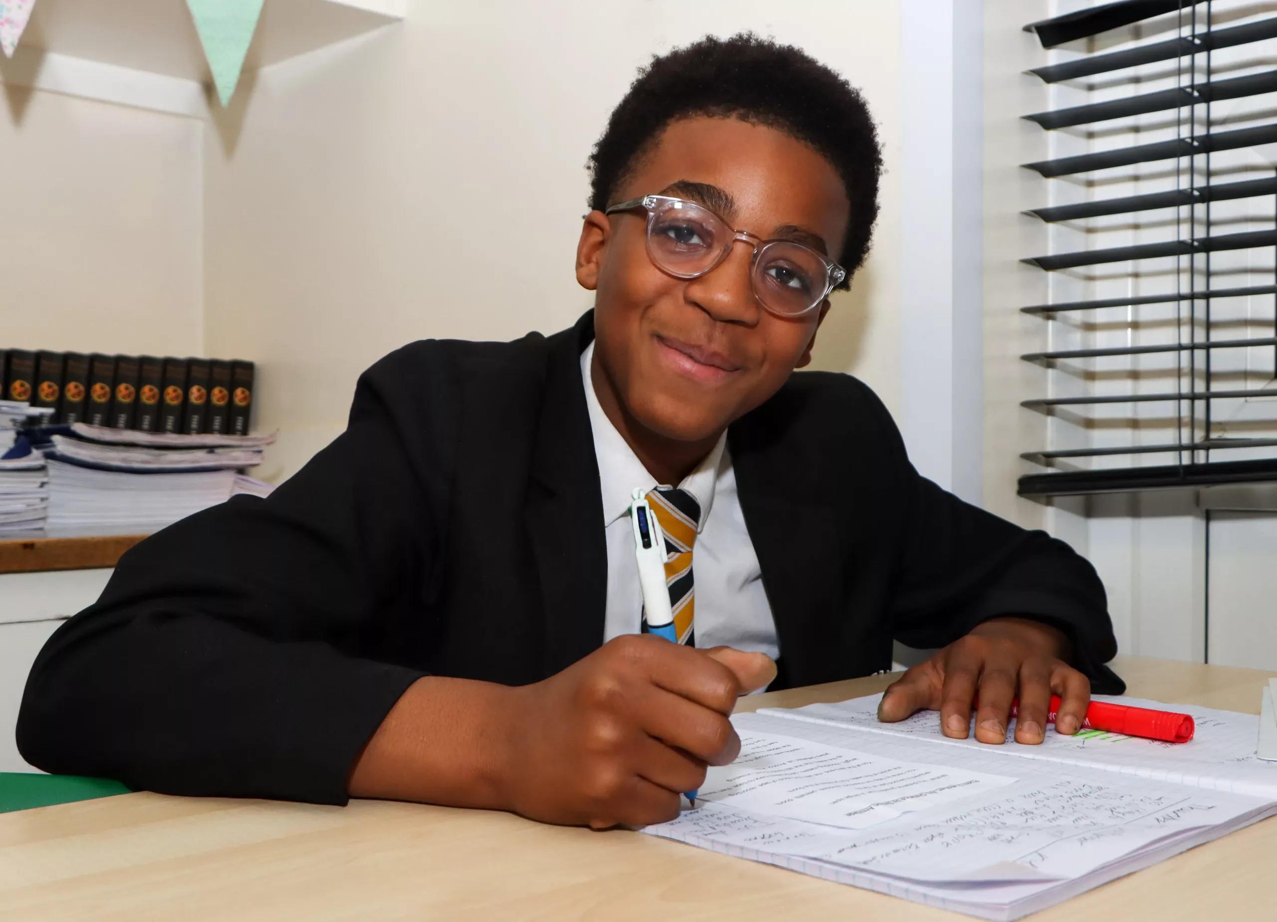 A boy smiling and writing in his book in lesson